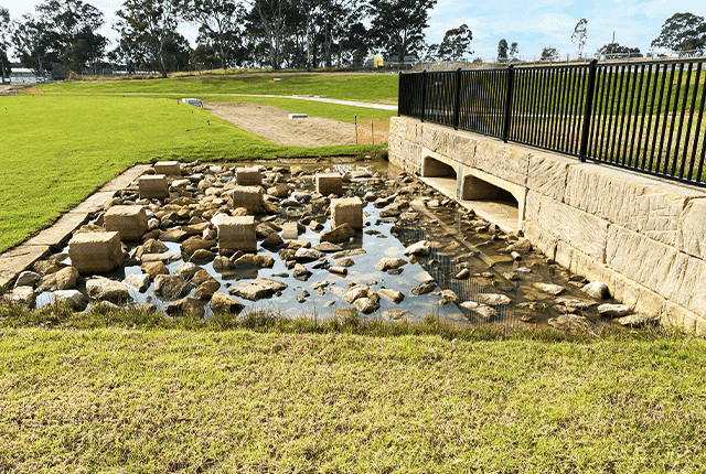 Drainage channel with rocks and concrete culverts for water flow management.