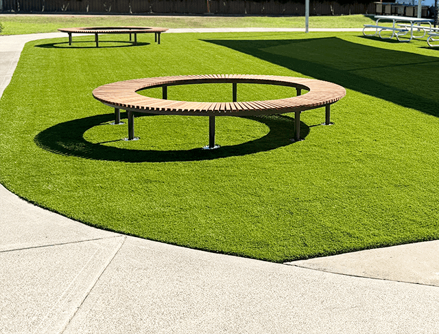 Circular park bench on well-maintained green lawn in outdoor public space.