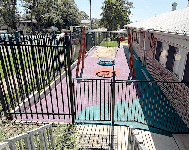 Childrens playground with secure fencing and colorful rubber safety surface.