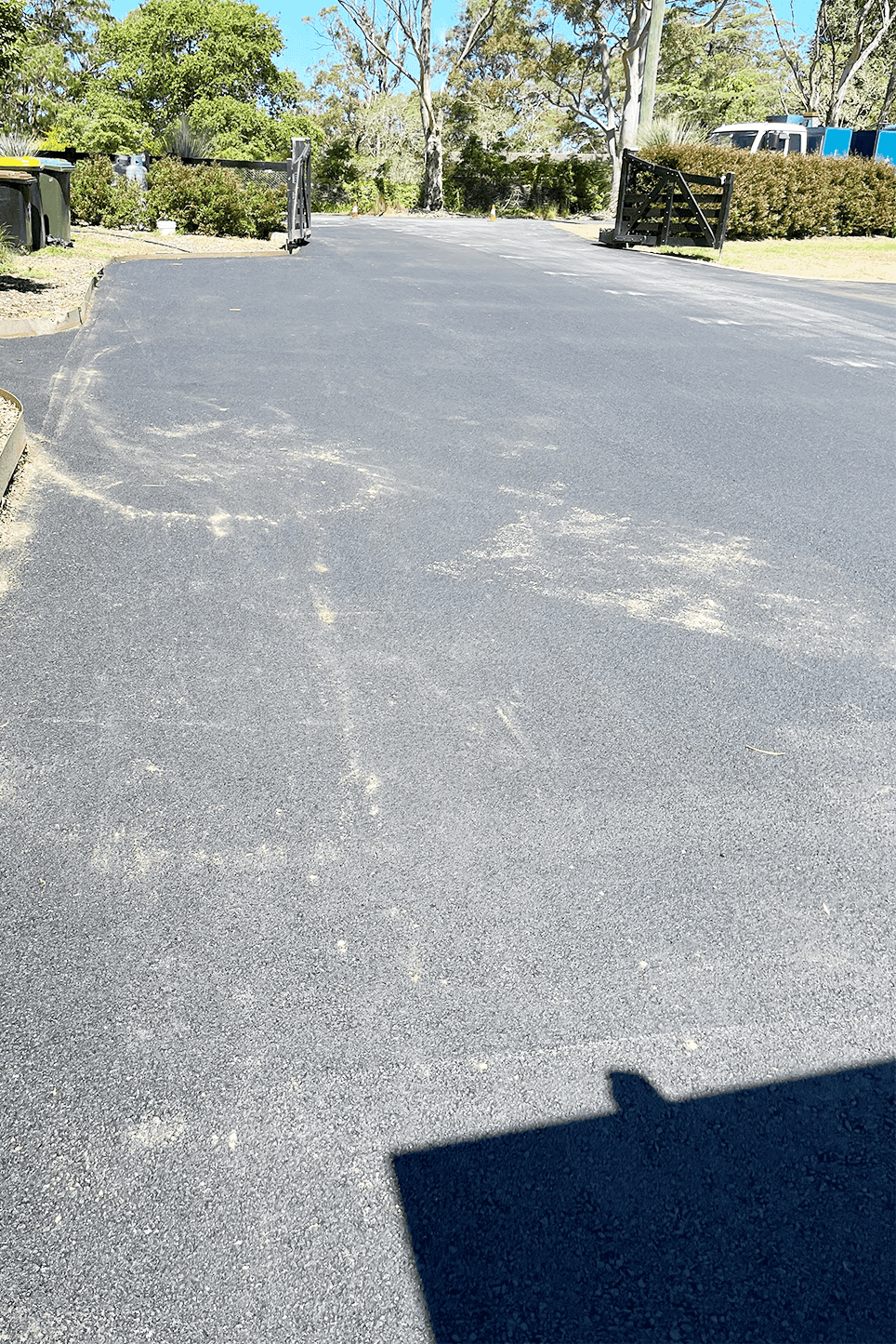 Freshly paved rural driveway with asphalt surface and wooden gates.