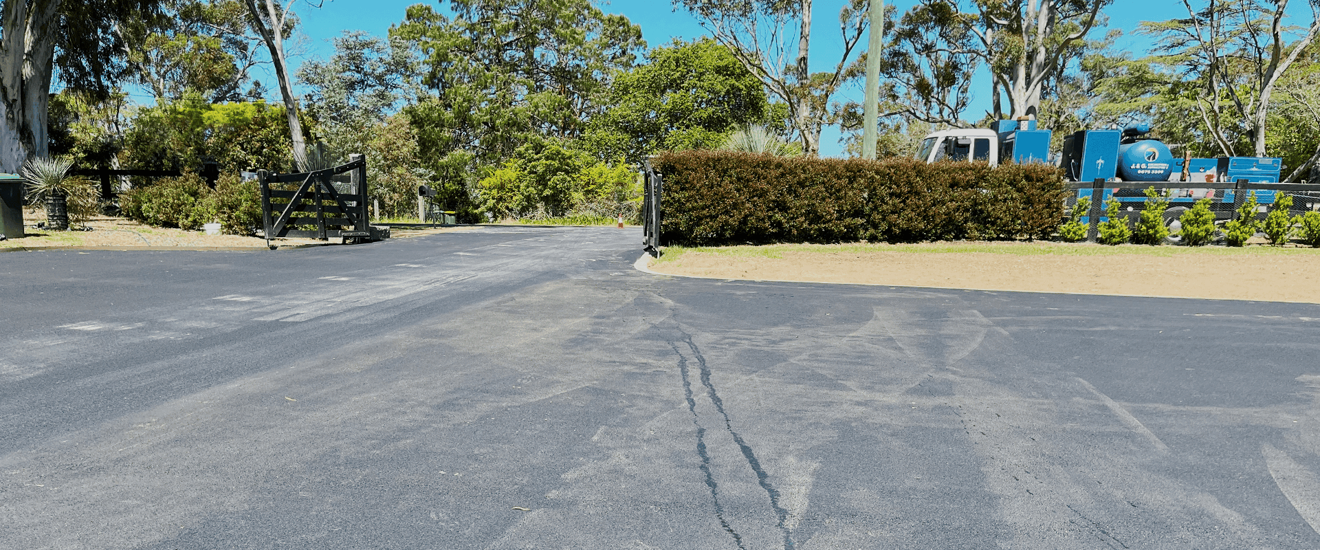 Newly paved rural driveway with asphalt surface and surrounding greenery.