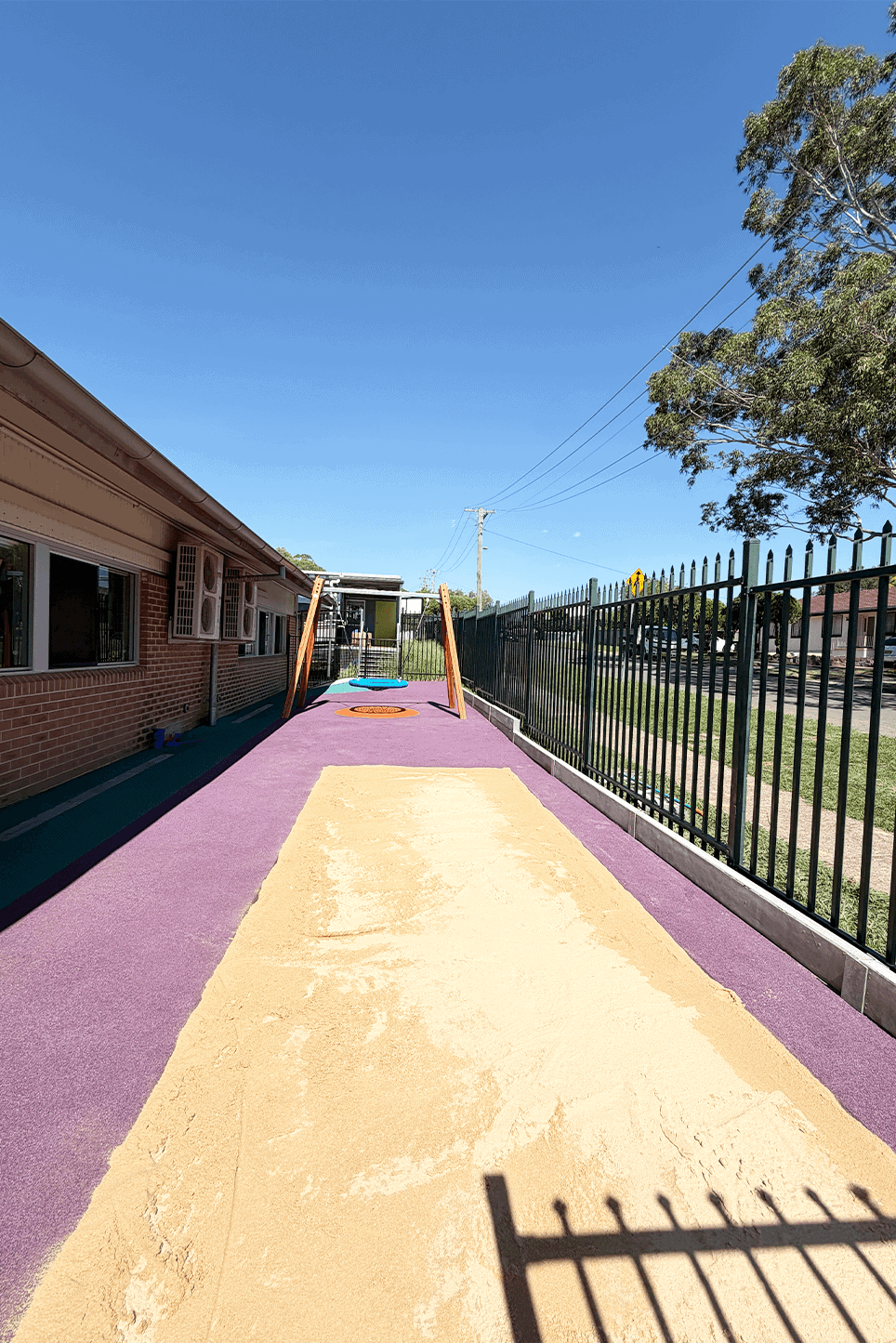 Newly constructed school playground with colorful rubber surface and safety fencing.