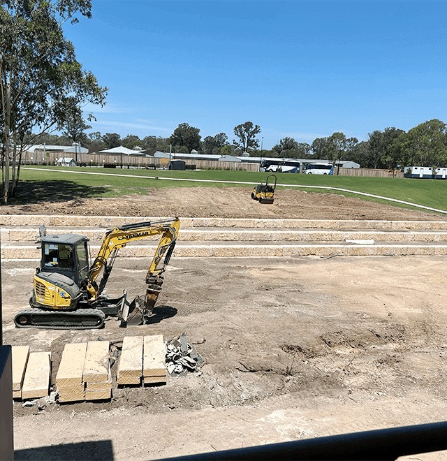 Construction site with excavator and paving materials under clear blue sky.