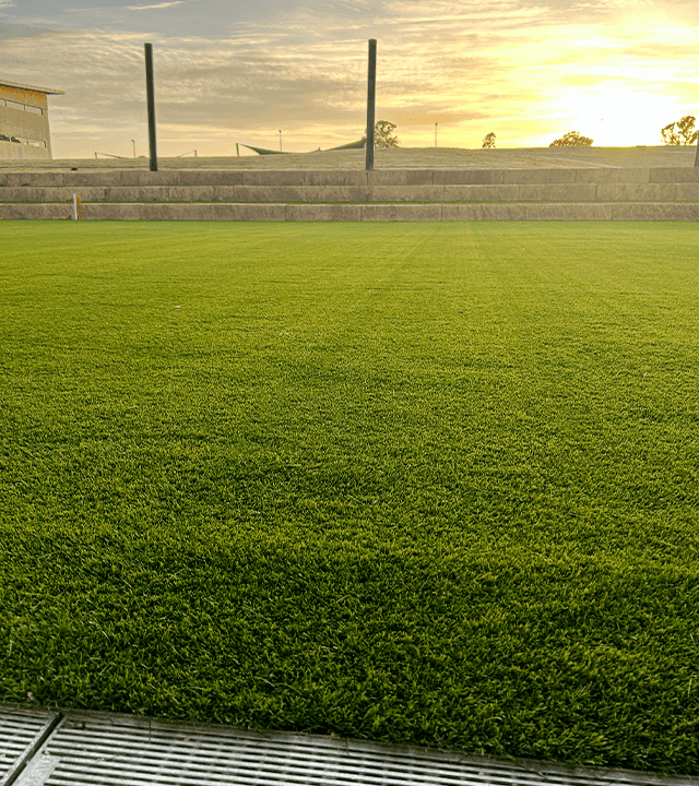 Well-maintained green sports field at sunset with seating area in the background.